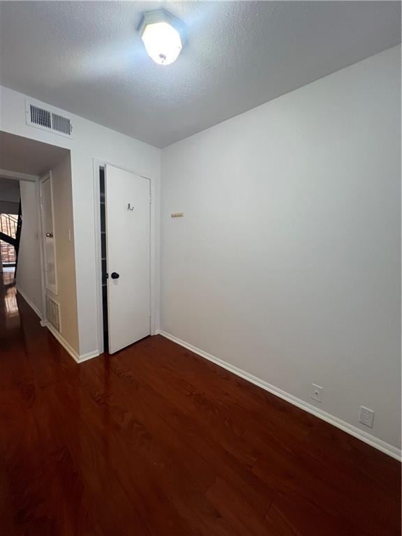 empty room featuring dark wood finished floors, visible vents, a textured ceiling, and baseboards