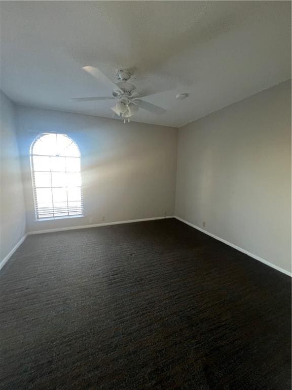 spare room with dark carpet, baseboards, and ceiling fan