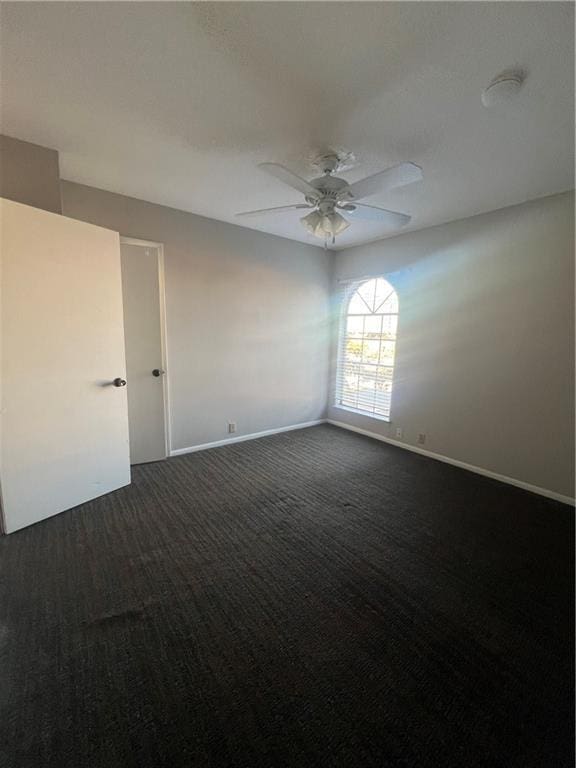 unfurnished room featuring baseboards, dark colored carpet, and ceiling fan