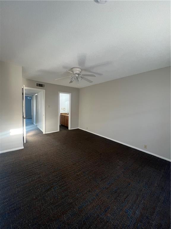 unfurnished room featuring dark carpet, a textured ceiling, baseboards, and a ceiling fan