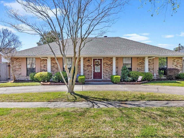 ranch-style house with a front lawn, roof with shingles, and brick siding