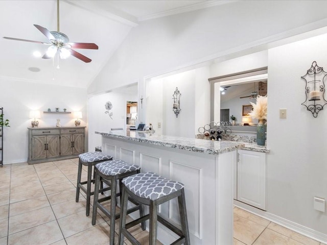 kitchen featuring lofted ceiling with beams, light tile patterned floors, light stone counters, and a kitchen breakfast bar