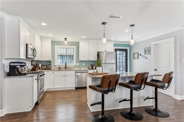 kitchen featuring visible vents, appliances with stainless steel finishes, a sink, a kitchen island, and a kitchen breakfast bar