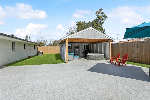 back of house featuring a hot tub, a fenced backyard, a yard, a patio area, and outdoor lounge area