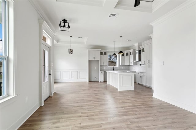 kitchen featuring visible vents, white cabinets, ornamental molding, wall chimney range hood, and a center island