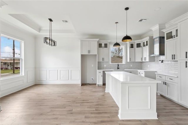 kitchen featuring wall chimney range hood, visible vents, a raised ceiling, and backsplash