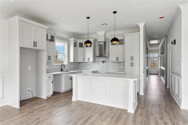 kitchen with tasteful backsplash, wall chimney range hood, light wood-style floors, and a center island