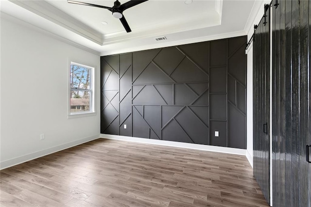 spare room featuring a barn door, wood finished floors, a ceiling fan, baseboards, and a tray ceiling