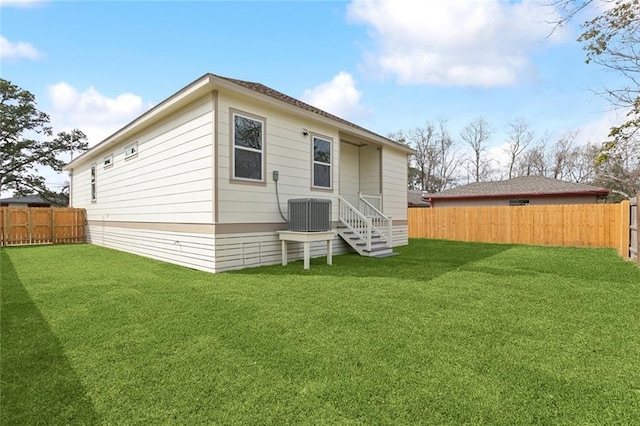 back of house featuring a fenced backyard, a yard, and central AC