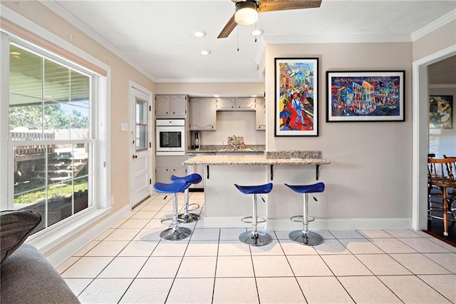 kitchen with light tile patterned floors, oven, a peninsula, a kitchen breakfast bar, and crown molding