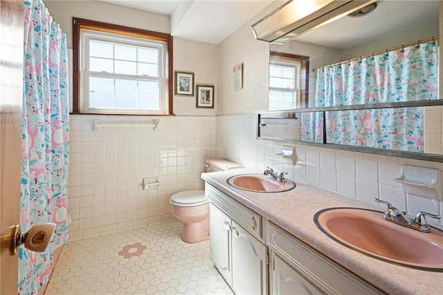 bathroom with a sink, tile walls, toilet, and double vanity