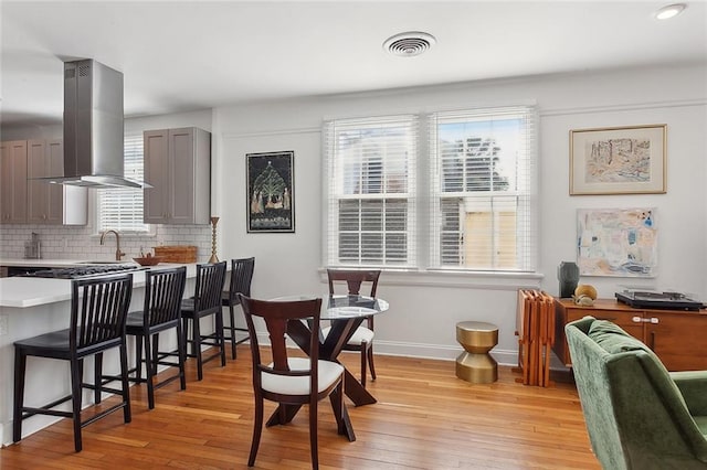 interior space with light wood finished floors, a breakfast bar, gray cabinets, and island range hood