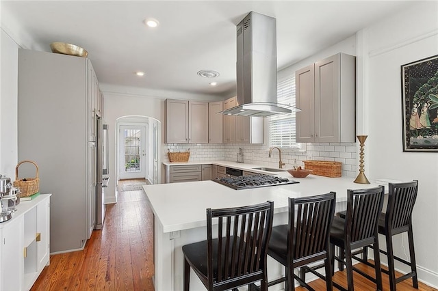 kitchen featuring gray cabinetry, a peninsula, arched walkways, and island range hood