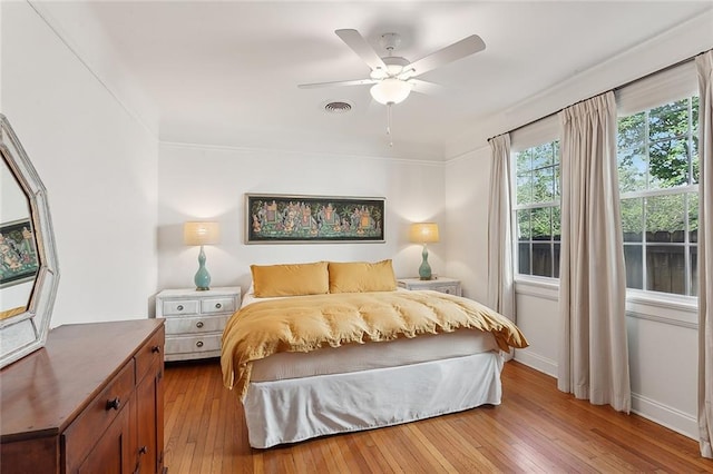 bedroom with wood-type flooring, visible vents, ornamental molding, ceiling fan, and baseboards