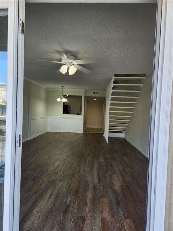 unfurnished living room with a textured ceiling, visible vents, a ceiling fan, ornamental molding, and dark wood finished floors