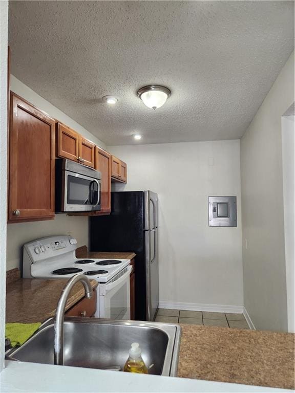 kitchen with electric stove, light tile patterned floors, stainless steel microwave, brown cabinetry, and a sink