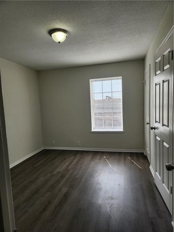 empty room with dark wood-style floors, a textured ceiling, and baseboards