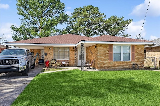 ranch-style home featuring driveway, roof with shingles, fence, a front yard, and brick siding