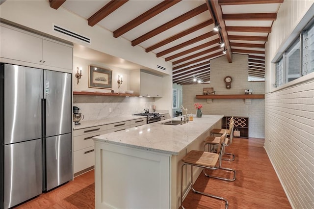 kitchen featuring open shelves, visible vents, lofted ceiling with beams, a sink, and stainless steel fridge