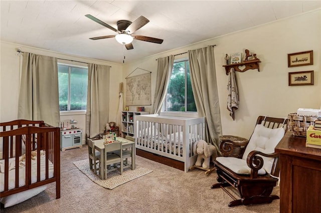 carpeted bedroom with ornamental molding, ceiling fan, and a crib