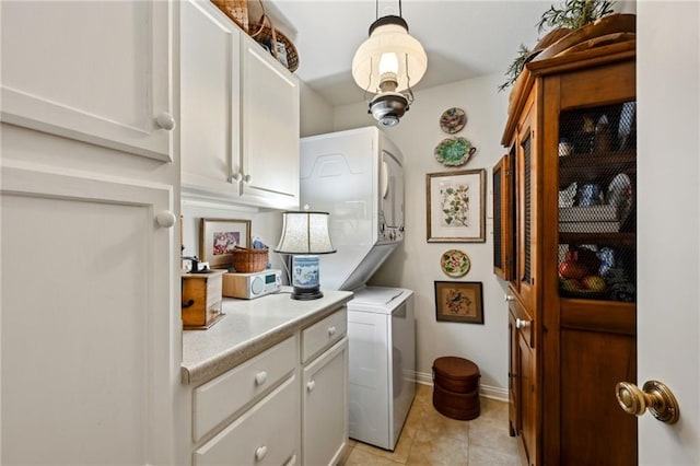 laundry room with cabinet space, light tile patterned floors, baseboards, and stacked washer / drying machine