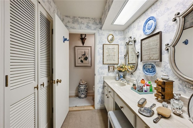 bathroom with wallpapered walls, baseboards, toilet, vanity, and a closet