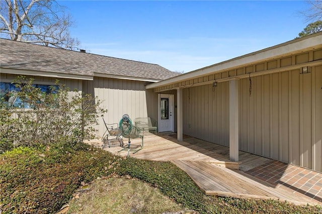 view of exterior entry with a wooden deck, a shingled roof, and fence