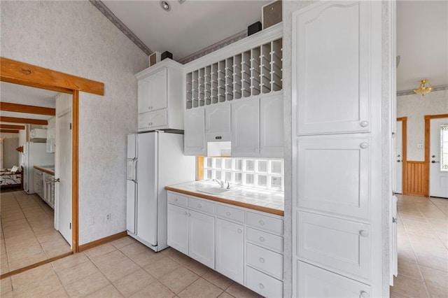 kitchen with white cabinets, wallpapered walls, white refrigerator with ice dispenser, and tile counters