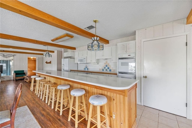 kitchen with visible vents, backsplash, beamed ceiling, light countertops, and white appliances