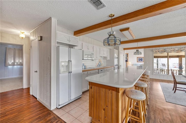 kitchen featuring white appliances, a breakfast bar, beam ceiling, light countertops, and backsplash