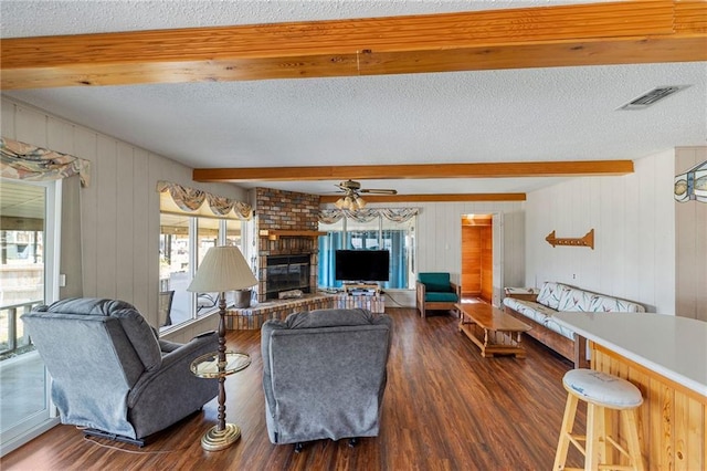 living room with wood finished floors, a brick fireplace, visible vents, and beamed ceiling