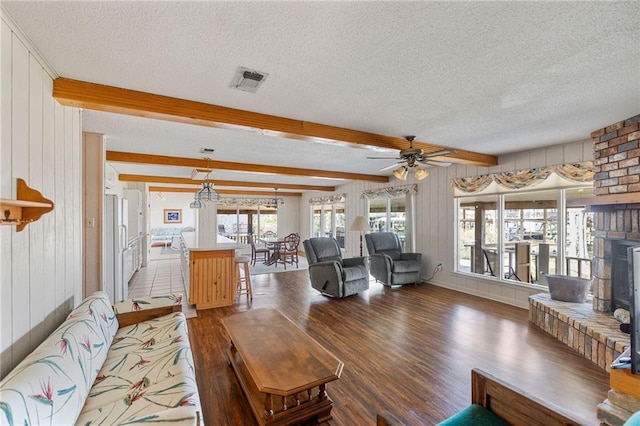 living area with visible vents, beam ceiling, a fireplace, wood finished floors, and a textured ceiling