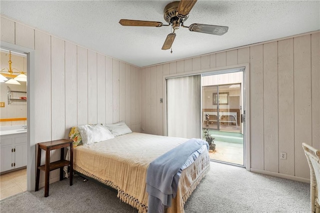 bedroom featuring ceiling fan, wood walls, a textured ceiling, access to outside, and light colored carpet