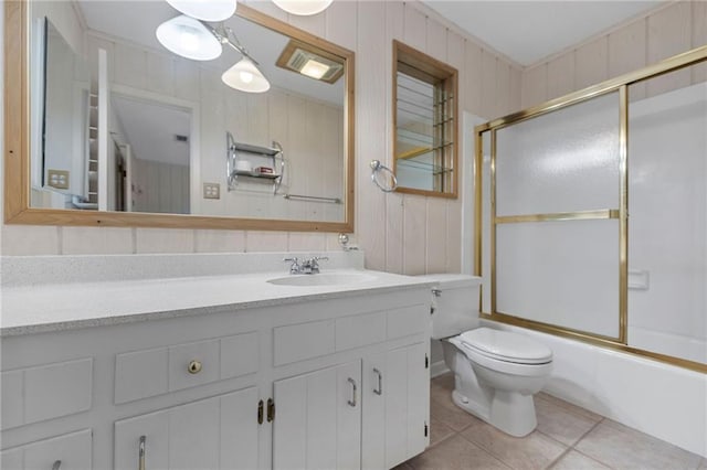 bathroom featuring toilet, wood walls, tile patterned flooring, enclosed tub / shower combo, and vanity