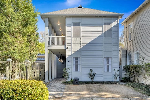 view of front of home with a shingled roof, a patio area, fence, and a balcony