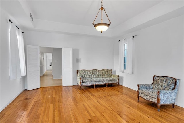 living area featuring light wood-type flooring, a raised ceiling, visible vents, and baseboards