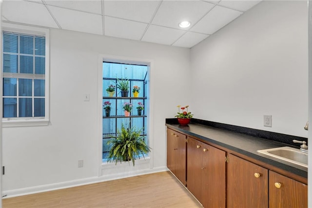 kitchen featuring brown cabinets, dark countertops, a paneled ceiling, a sink, and light wood-type flooring