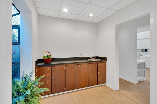 bar featuring light wood-style flooring, baseboards, a drop ceiling, and a sink