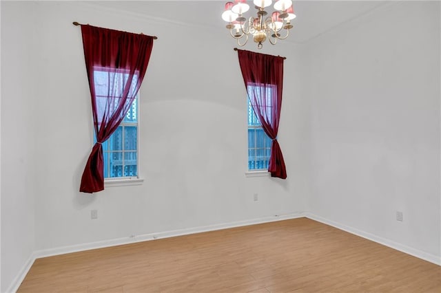 spare room with an inviting chandelier, baseboards, and wood finished floors