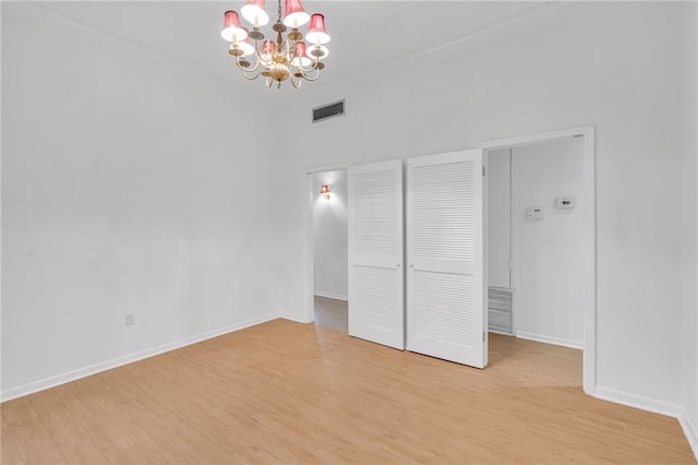 unfurnished bedroom featuring visible vents, a notable chandelier, light wood-style flooring, and baseboards