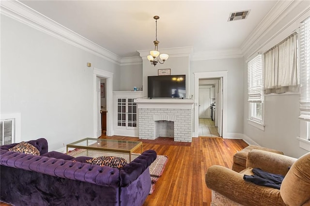 living area with baseboards, visible vents, ornamental molding, wood finished floors, and a fireplace