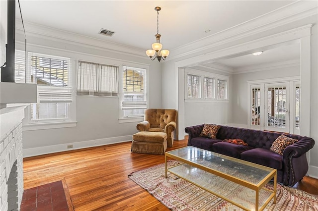 living area featuring a notable chandelier, visible vents, ornamental molding, wood finished floors, and baseboards