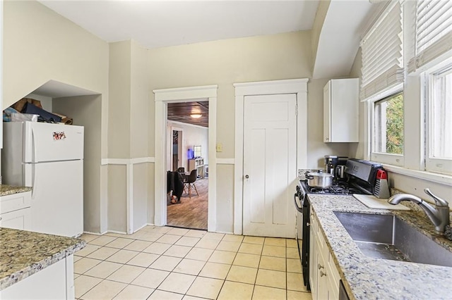 kitchen with light tile patterned floors, a sink, white cabinetry, freestanding refrigerator, and gas range oven