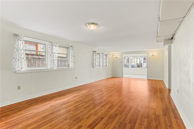 empty room with a wealth of natural light, light wood-style flooring, and baseboards