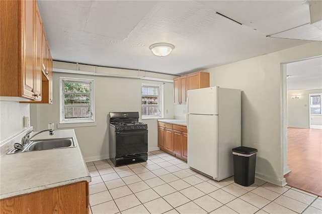 kitchen with light tile patterned floors, light countertops, freestanding refrigerator, gas stove, and a sink