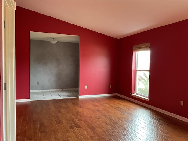 empty room featuring lofted ceiling, baseboards, and wood finished floors