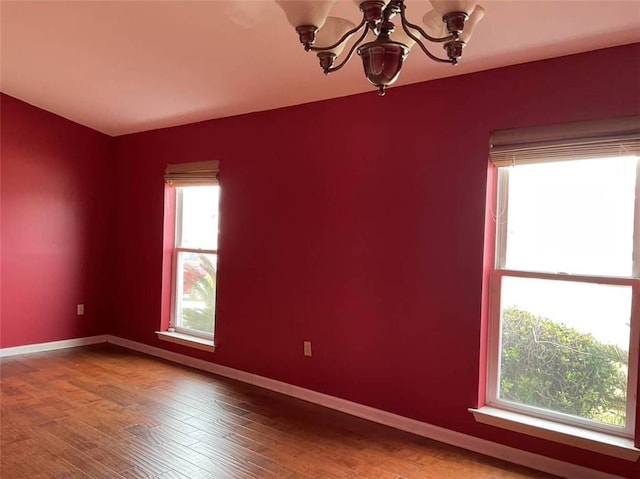 unfurnished room featuring a chandelier, baseboards, and wood finished floors