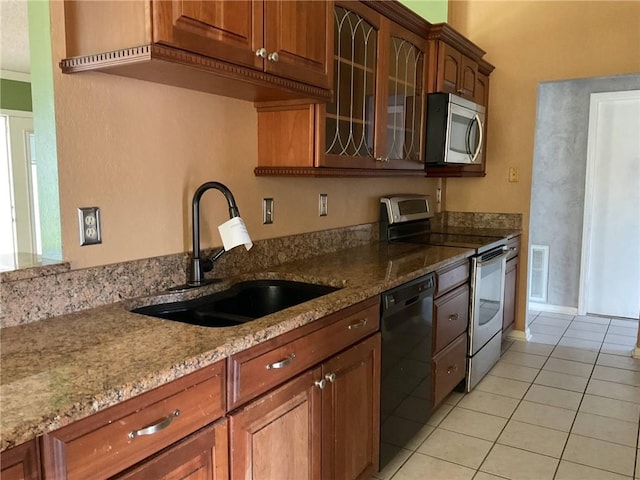 kitchen featuring a sink, light stone counters, appliances with stainless steel finishes, light tile patterned flooring, and glass insert cabinets