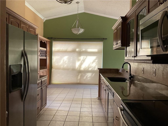 kitchen with dark countertops, vaulted ceiling, ornamental molding, appliances with stainless steel finishes, and a sink