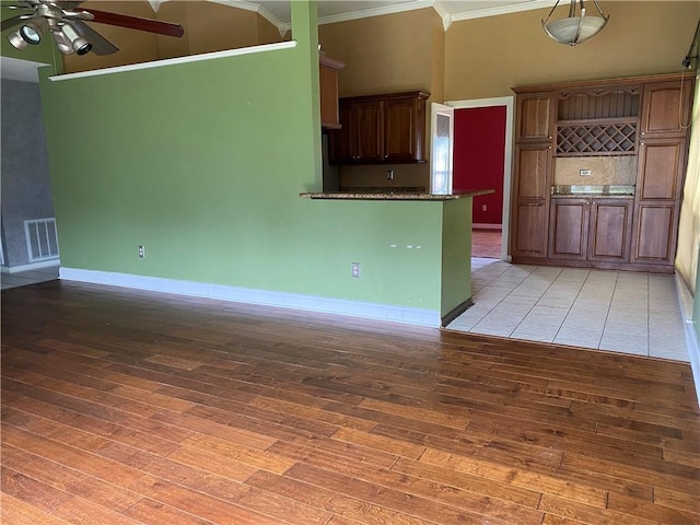 kitchen with visible vents, a ceiling fan, light wood-style floors, a high ceiling, and crown molding